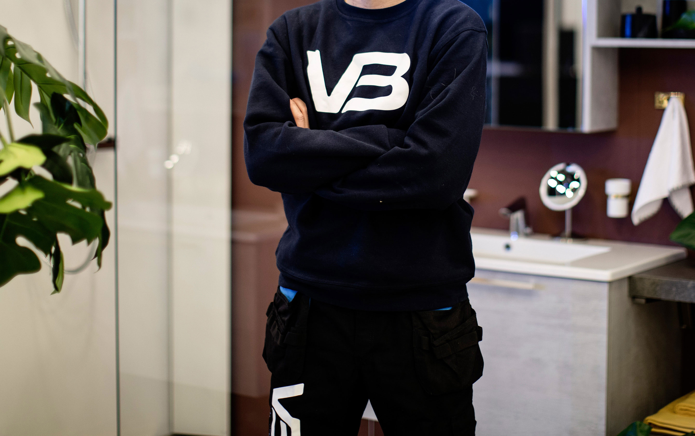 VB-rørlegger med armene i kors og VB logo på genseren foran servantskap med hvit servant på burgunder vegg.